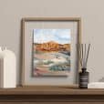 A print of "The Vista" painting of a desert scene displayed in a frame